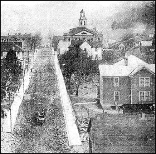 In 1898 construction began on the courthouse seen at the top center of this picture. Apparently the building was located on the site of the first one. A bell in the large cupola called jurors to court. This view is from the end of Main Street, just across the Kentucky River from present-day Fields Cliff. Wooden sidewalks are on both sides of the street. This photo was taken sometime after 1907.